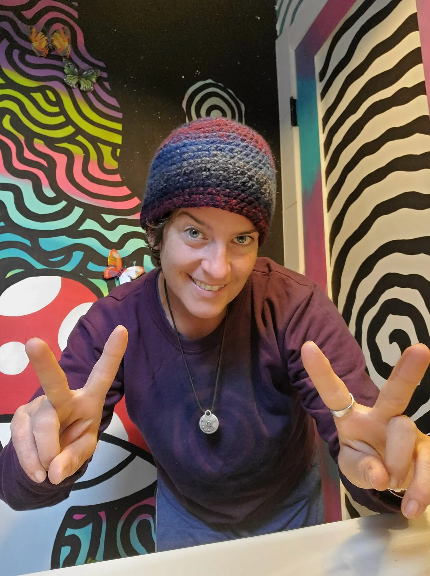 Cheryl smiling and flashing peace signs in front of a painted mural